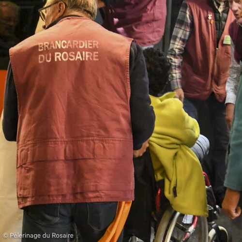 Brancardier du Rosaire aidant un pèlerin en fauteuil roulant.