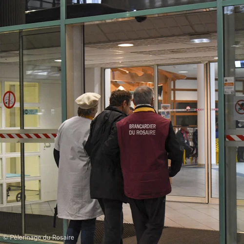 Brancardier du Rosaire aide pèlerin à entrer.